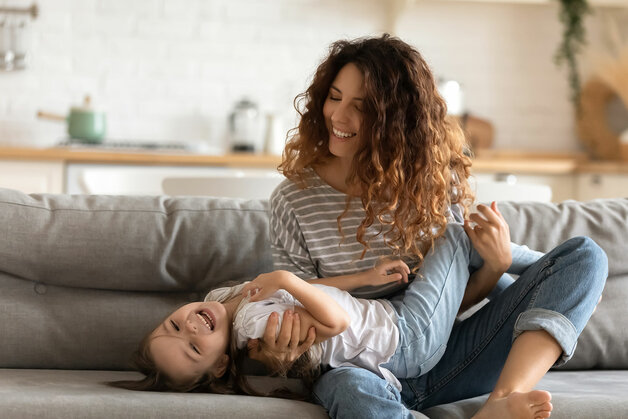 Mutter und Tochter spielen auf dem Sofa im Wohnzimmer des neuen massiven Traumhauses